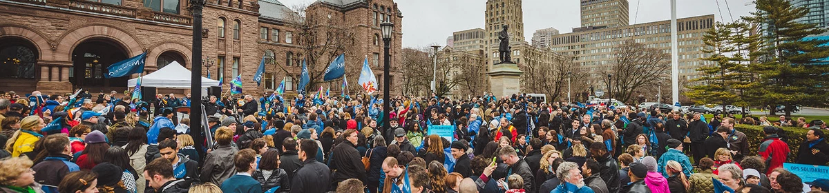 Crowd waving Pride flags and AMAPCEO flags in front of Queen's Park
