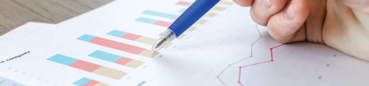 A hand holding a pen writing on a documents with a series of graphs