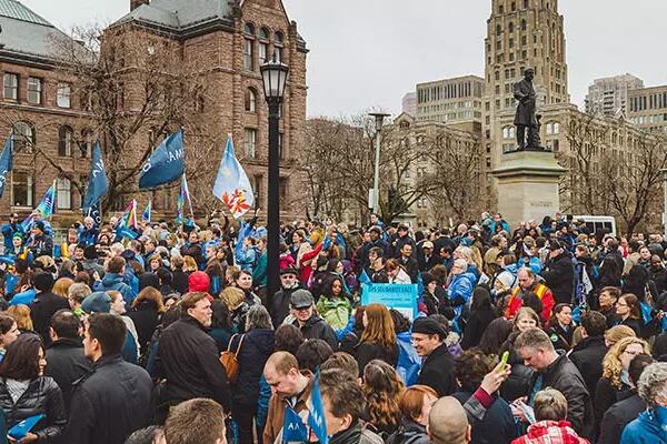 Crowd waving Pride flags and AMAPCEO flags in front of Queen's Park