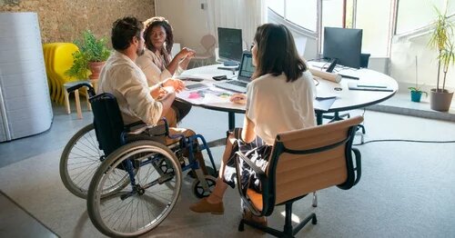 Group of people, one of whom is using a wheelchair, gathered around a conference table in an office