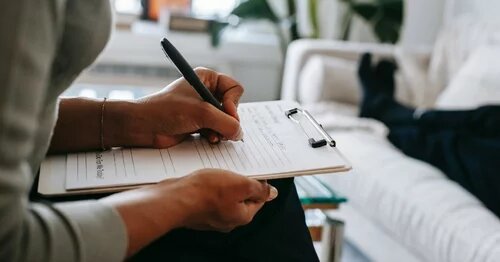 Photo of a hands holding a checklist with a person reclining in the background