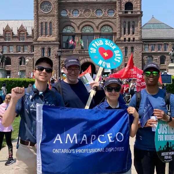 Activists holding an AMAPCEO flag and paid sick days sign in front of Queen's Park