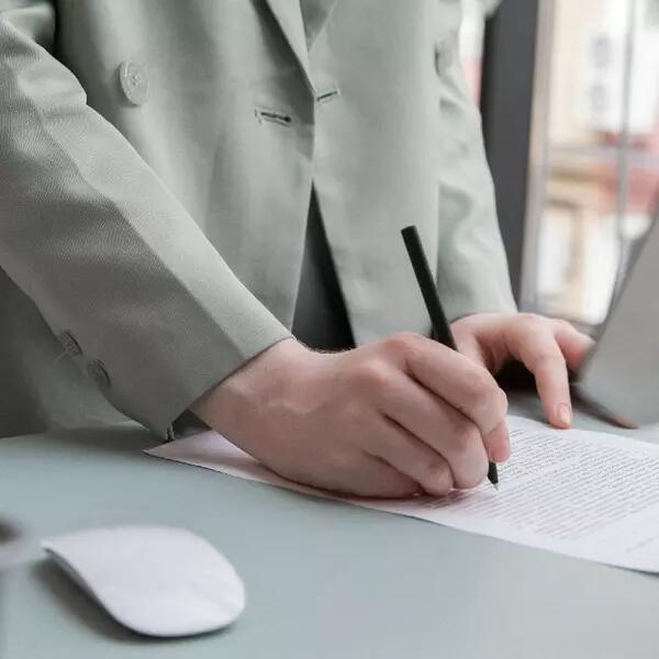 A person's hands taking notes on a paper with a monitor and mouse on the desk