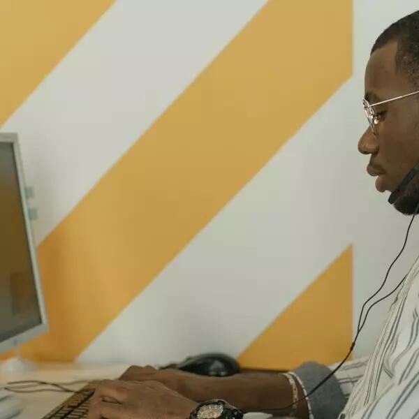 A person in an office typing on a laptop wearing a headset
