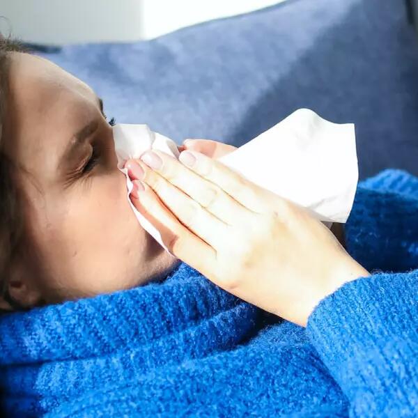 A person lying on a couch blowing their nose